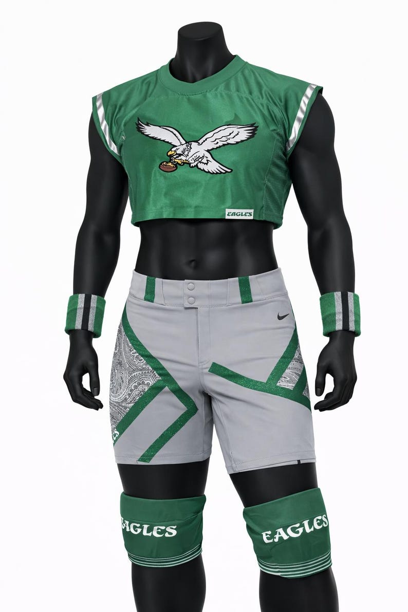 May include: A green cropped jersey with an eagle graphic and the text EAGLES, paired with grey athletic shorts featuring green and paisley accents. The outfit includes green wristbands and green knee pads with the text EAGLES printed on them.
