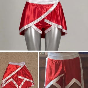 May include: Bright red satin athletic shorts featuring a wide white elastic waistband and white trim detailing along the overlapping front panels. The shorts have a short, flared cut with a smooth, shiny finish and distinct white geometric accents.