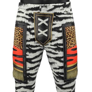 May include: White pants with a black zebra stripe pattern featuring a central black shield patch with two white X symbols. The sides include rectangular panels with leopard print, bright orange sections, gold trim, and olive green fringe accents.