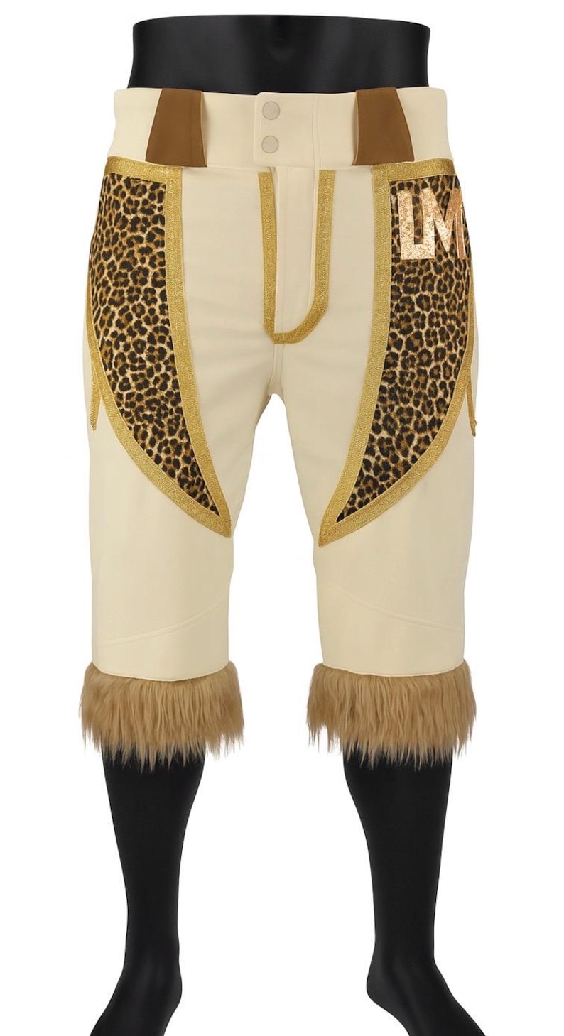 May include: Cream-colored baseball pants featuring leopard print panels on the hips, gold trim, and brown faux fur cuffs at the hem. The pants include a button closure at the waist and the letters LM in gold on the upper left leopard print panel.