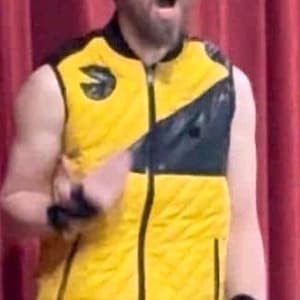 May include: A sleeveless quilted vest featuring a vibrant yellow base with black accents, a full-length front zipper, and a circular black logo patch on the upper right chest. The garment has a high collar and a structured, athletic design.