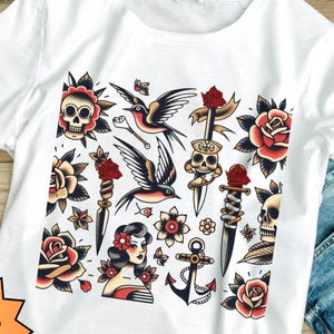 May include: White t-shirt with a colorful old school tattoo design featuring a skull, dagger, anchor, roses, and a bird.