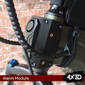 May include: A black alarm module with a silver speaker and gold screws attached to a black and green electric scooter. The alarm module is labeled "Alarm Module".