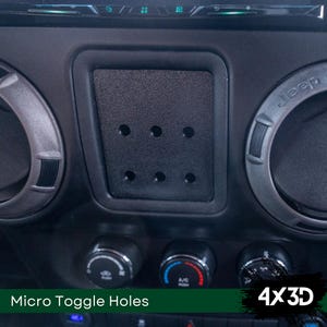 Può includere: Primo piano di un cruscotto nero con un pannello rettangolare che presenta diversi fori rotondi. Il pannello è etichettato "Micro Toggle Holes". Il testo "4x3D" è visibile nell'angolo in basso a destra dell'immagine.