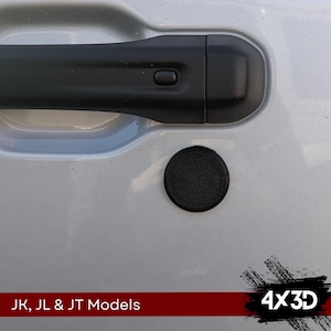 May include: A black round 4x3D emblem on a silver car door. The emblem is textured and has a raised 4x3D logo. The text "JK, JL & JT Models" is visible below the emblem.