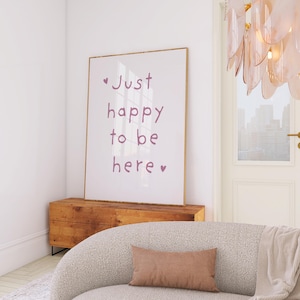 May include: A framed print with the words "Just happy to be here" in a soft purple hue hangs above a wooden cabinet. A curved, textured sofa with a brown rectangular pillow and a beige throw blanket is in the foreground. A decorative chandelier hangs from the ceiling.