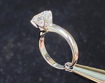 May include: A silver engagement ring with a large, round, clear diamond. The ring is marked "G750" on the inside of the band.