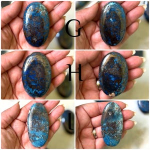 May include: Oval-shaped azurite stones with a mix of deep blue and brown hues. The stones have a polished, smooth surface and are held in a hand. The image shows several stones, each with unique color patterns.
