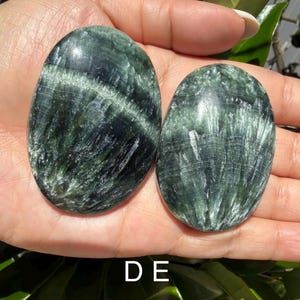 May include: Two oval-shaped, polished stones with a dark green and white striped pattern. The stones are smooth and appear to be natural gemstones. The image is well-lit, showcasing the details of the stones.