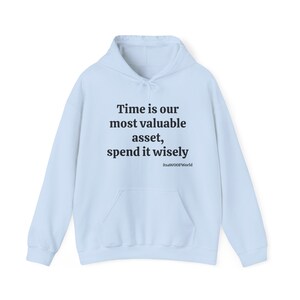 Pode incluir: Moletom azul claro com capuz com uma estampa preta que diz "Time is our most valuable asset, spend it wisely" e "itsaWOOFWorld" em uma fonte menor.
