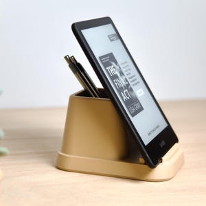 May include: A beige desktop organizer with a black e-reader propped up against it. The e-reader is displaying the title "The Final Act" by Lisa Gray. Two black pens are in the organizer.
