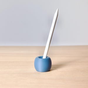 May include: A blue ceramic pencil holder with a white pencil standing upright in it.