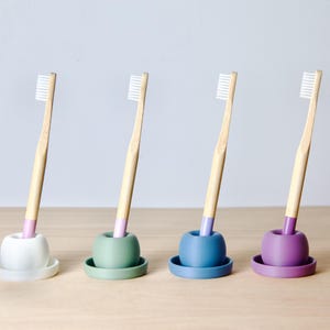 Puede incluir: Cuatro cepillos de dientes de bambú con bases de silicona de diferentes colores. Las bases son blancas, verdes, azules y moradas.