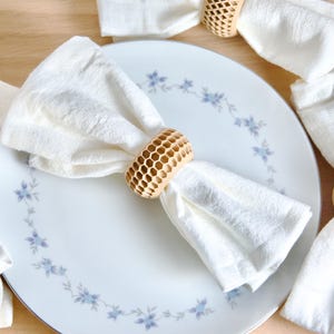 以下が含まれることがあります： 木製のナプキンリングが付いた白い布ナプキンが4枚。リングはハニカム模様です。ナプキンは青い花柄の白いプレートの上に置かれています。