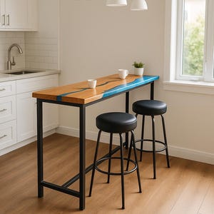 May include: A rectangular bar table with a natural wood top featuring a blue resin inlay, supported by a black metal frame. Two black round stools with metal legs are positioned underneath the table. Two white mugs sit on the tabletop.