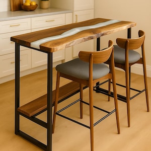 Op de afbeelding: Een rechthoekige houten bar-tafel met een centrale witte harsinleg, ondersteund door een zwart metalen frame met een onderste plank, vergezeld door twee houten barkrukken met gebogen rugleuningen en grijze gestoffeerde zittingen.