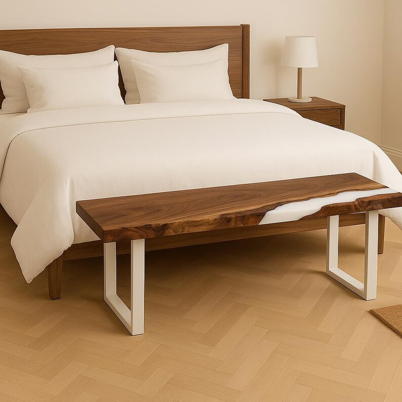 May include: A wooden bench with a live edge design and a white resin inlay. The bench has a dark brown finish and sits on white metal legs. The bench is placed at the foot of a bed with white bedding.