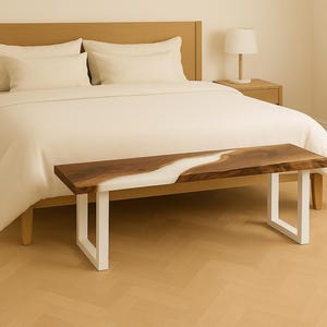 K&ouml;nnte beinhalten: Schlafzimmer mit Holzbett und cremefarbener Bettw&auml;sche. Am Fu&szlig;ende des Bettes befindet sich eine Bank mit einer Walnussplatte und wei&szlig;en Beinen. Die Bank hat ein wei&szlig;es Harz-Fluss-Design. Die Bank ist ca. 150 cm lang.