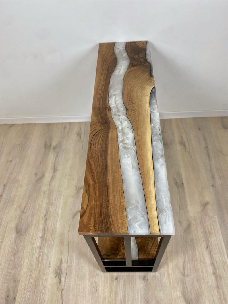 May include: A wooden bench with a live edge design and a river of white resin running through the center. The bench has a dark metal frame. The wood has a natural grain and a warm brown color.