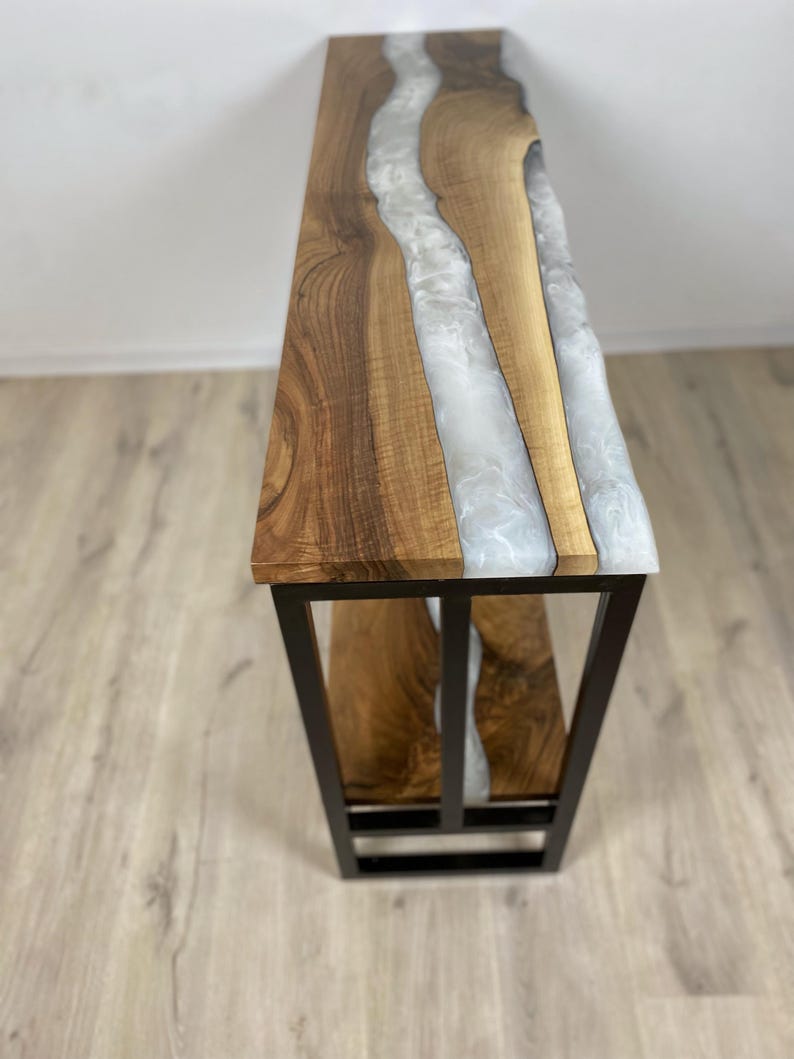 May include: A handcrafted console table with a live edge walnut top and a white epoxy resin river. The table has a black metal base and a natural wood grain finish. The table is approximately 48 inches long.