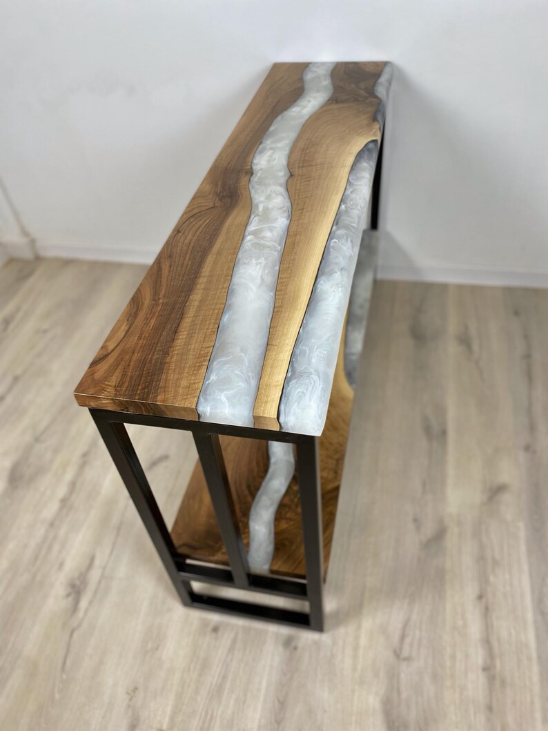 May include: A wooden console table with a river of white resin flowing through the center. The table has a dark metal frame and a lower shelf. The wood has a natural grain, and the resin has a glossy finish.