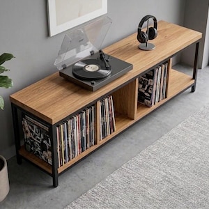 May include: A long rectangular media console featuring a light brown wood grain top and bottom shelf supported by a black metal frame. The unit includes three open storage compartments filled with vinyl records, a black turntable, and headphones.
