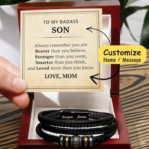 May include: A wooden box containing a message card that reads "To my badass son, Always remember you are braver than you believe, stronger than you seem, smarter than you think, and loved more than you know. Love, Mom." The box also contains a black leather bracelet with the words "love you forever" engraved on it.