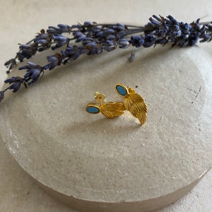 May include: Gold leaf earrings with blue oval stones. The earrings are delicate and feminine.