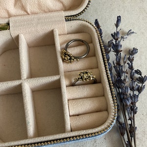 May include: A blue velvet jewelry box with two rings inside. The rings are made of silver and have gold accents. The box has a zipper closure and is lined with white velvet.
