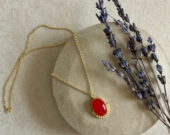May include: A gold chain necklace with a red oval pendant. The pendant is surrounded by small gold beads.