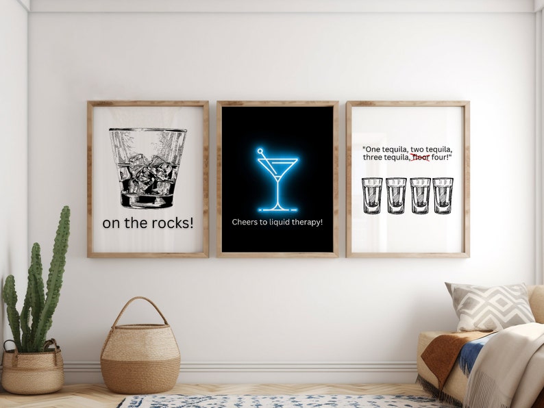May include: Three framed prints with black and white illustrations of cocktails. The first print shows a glass of whiskey on the rocks with the text "on the rocks!" The second print shows a martini glass with the text "Cheers to liquid therapy!" The third print shows four shot glasses with the text "One tequila, two tequila, three tequila, floor four!"