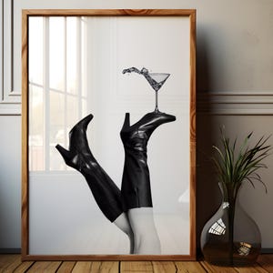 K&ouml;nnte beinhalten: Ein Schwarzwei&szlig;foto von einem Paar schwarzer Stiefel mit Abs&auml;tzen, die aufrecht stehen, wobei die Oberteile der Stiefel auf einem Martini-Glas ruhen. Das Glas ist mit Wasser gef&uuml;llt und es spritzt Wasser heraus.