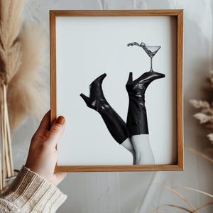 K&ouml;nnte beinhalten: Schwarzwei&szlig;foto von einem Paar schwarzer Stiefel mit Abs&auml;tzen, auf denen ein Martini-Glas balanciert.
