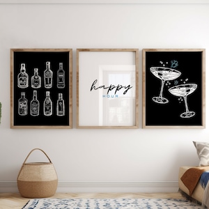 May include: Three black and white framed prints with a minimalist design. The left print features a collection of liquor bottles, the middle print says "happy hour" in cursive, and the right print shows two champagne flutes.