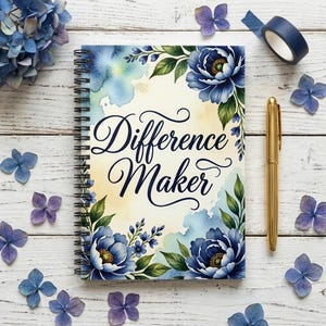 May include: A spiral-bound notebook with the words "Difference Maker" in script. The cover has blue floral designs and green leaves in a watercolour style. A gold pen and blue washi tape are placed nearby, with scattered blue and purple flower petals.