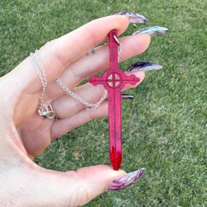 May include: A red sword pendant necklace with a silver chain. The sword has a circular design at the top and a pointed tip.
