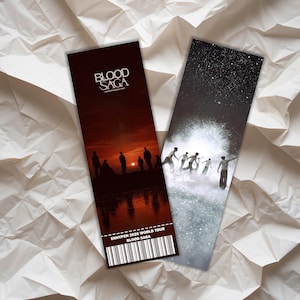 Puede incluir: Dos marcapáginas con el texto "BLOOD SAGA" y "ENHYPEN 2026 WORLD TOUR BLOOD SAGA". Uno presenta una escena de puesta de sol con siluetas. El otro muestra figuras en un cielo estrellado.
