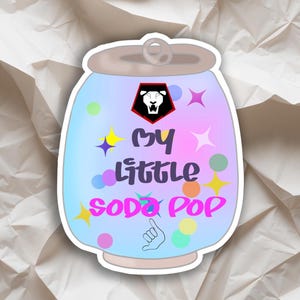 Może przedstawiać: Naklejka w kształcie puszki po napoju gazowanym z jasnoniebieskim i fioletowym gradientem. Tekst "My Little Soda Pop" znajduje się na środku, z kolorowymi gwiazdkami i kropkami. Gest dłoni znajduje się na dole.