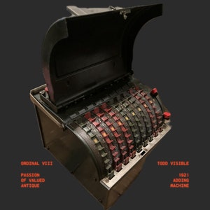 Puede incluir: Una máquina de sumar vintage negra y plateada con una pantalla de números rojos y negros. La máquina está abierta y la parte superior está levantada. El texto "ORDINAL VIII PASSION OF VALUED ANTIQUE" es visible en el lado izquierdo de la máquina. El texto "TODD VISIBLE 1921 ADDING MACHINE" es visible en el lado derecho de la máquina.