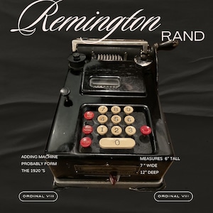 Op de afbeelding: Een zwarte Remington Rand rekenmachine met een rood-wit toetsenbord. De machine is 15 cm hoog, 18 cm breed en 30 cm diep. De machine is gelabeld met "Adding Machine, Probably Form, The 1920's".