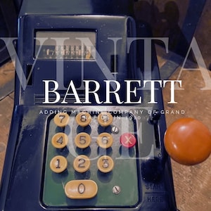 May include: Vintage black cash register with a white label that reads "Barret Adding Machine Company of Grand Rapids in 1910". The register has a number display, a lever, and a round orange button.