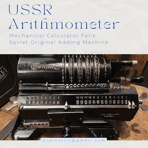 Puede incluir: Una calculadora mecánica negra con la palabra "Феликс" en la parte delantera. La calculadora tiene una serie de diales numerados y una palanca en el lado derecho. La calculadora está etiquetada como "3-д СЧЕТНАЯ  ГКУРСК".