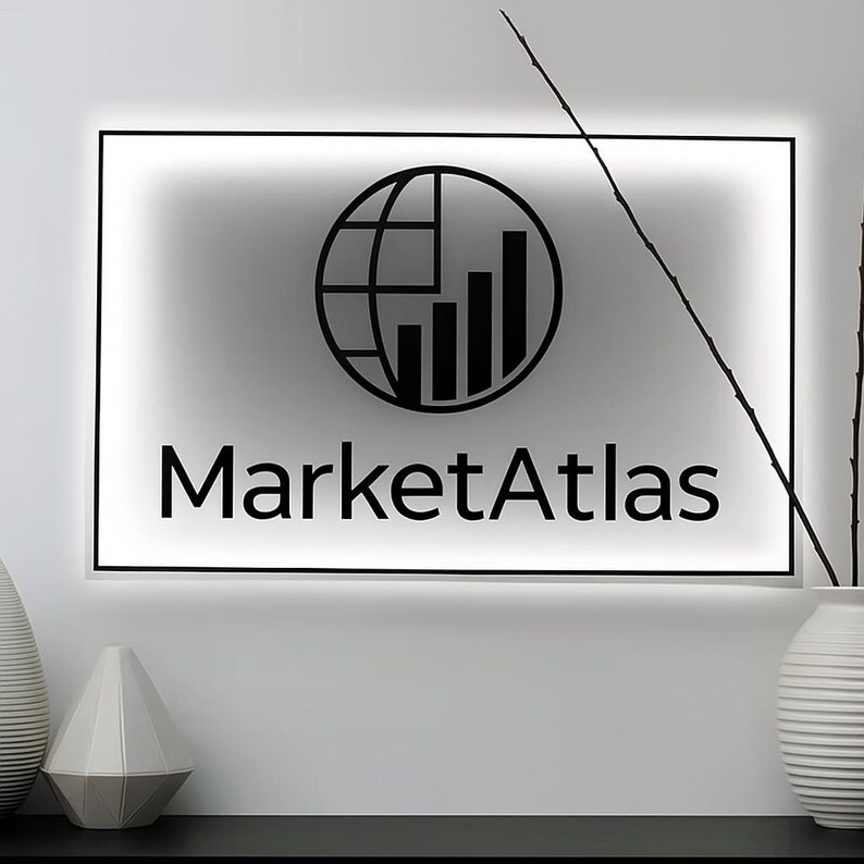 Op de afbeelding: Een verlicht bord met de tekst "MarketAtlas" in een modern zwart lettertype. Boven de tekst staat een zwarte afbeelding van een wereldbol met een staafdiagram. Het bord is zwart omlijst en aan een witte muur bevestigd.