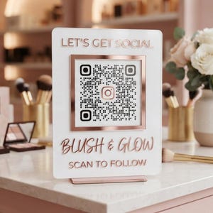 May include: A rectangular white acrylic sign with rose gold lettering and a matching frame. The text reads LET'S GET SOCIAL, BLUSH & GLOW, and SCAN TO FOLLOW. A central QR code features an Instagram icon, and the sign stands on a rose gold base.