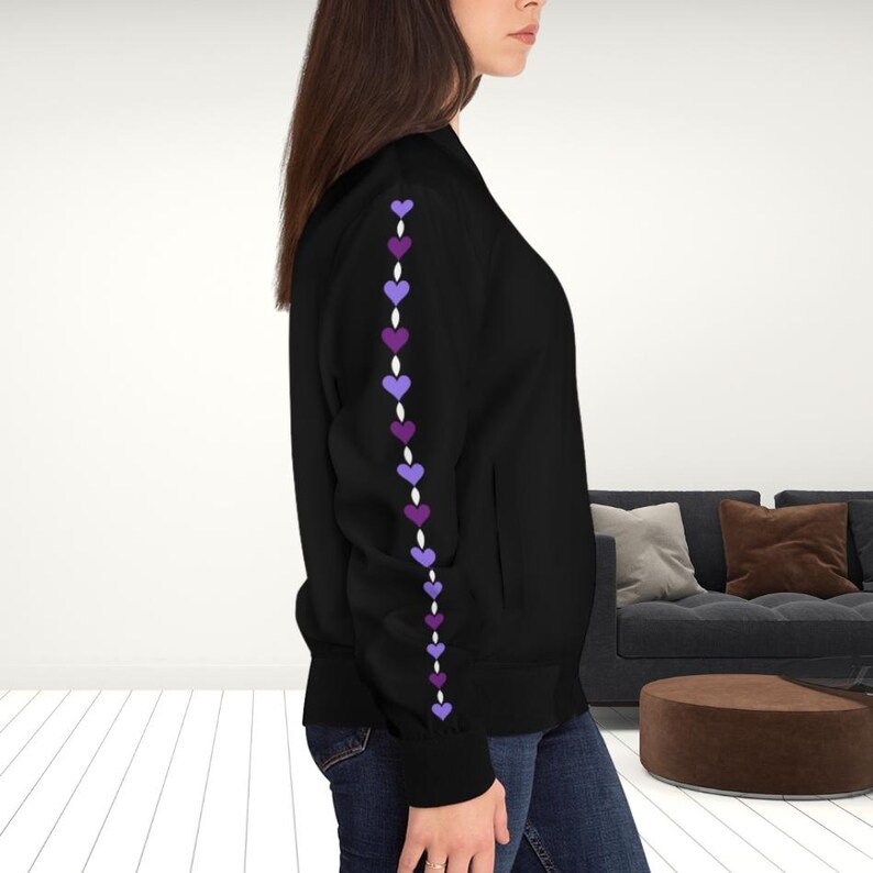 May include: Black bomber jacket with a row of purple hearts down the left sleeve. The hearts are in varying shades of purple and are connected by a white dotted line. The jacket has a ribbed cuff and a pocket.