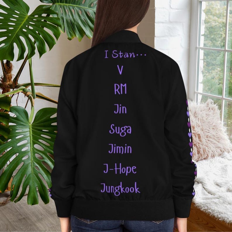 May include: Black bomber jacket with purple text that reads "I Stan..." followed by names. The jacket has a purple heart pattern on the sleeve. The jacket is shown from the back.