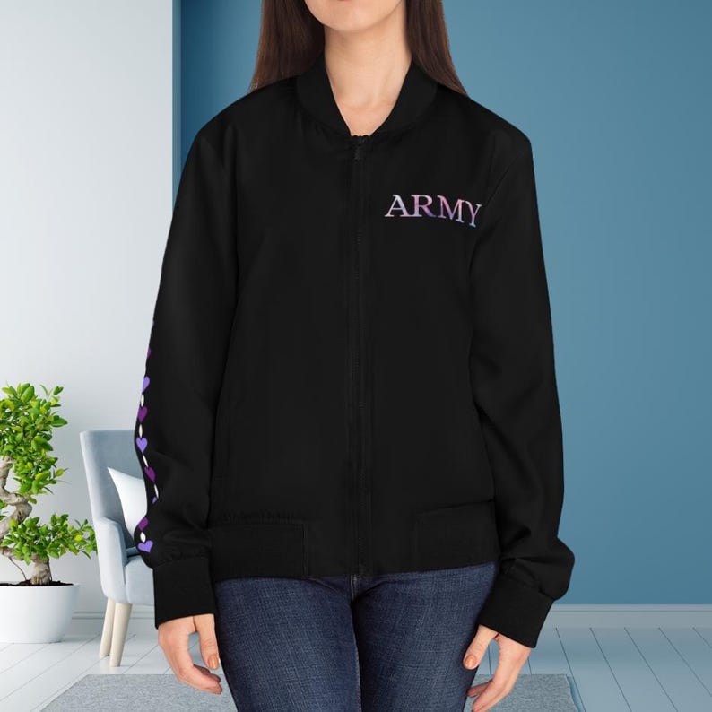 May include: Black bomber jacket with the word "ARMY" in purple script on the chest. The left sleeve features a pattern of purple hearts. The jacket has a zipper closure and two front pockets. The model is wearing blue jeans.