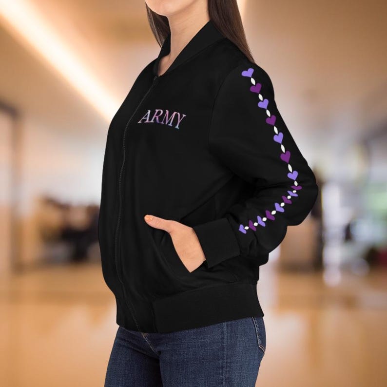 May include: Black bomber jacket with the word "ARMY" embroidered in purple on the chest. The left sleeve features a line of purple and white heart-shaped designs. The jacket has a full-length zipper and two front pockets.