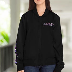 May include: Black bomber jacket with the word "ARMY" in purple and white lettering on the chest. The left sleeve features a design of purple and white hearts. The jacket has a zipper closure and two front pockets.