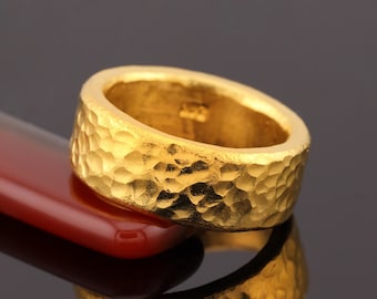 May include: A gold ring with a hammered texture. The ring is thick and has a wide band.